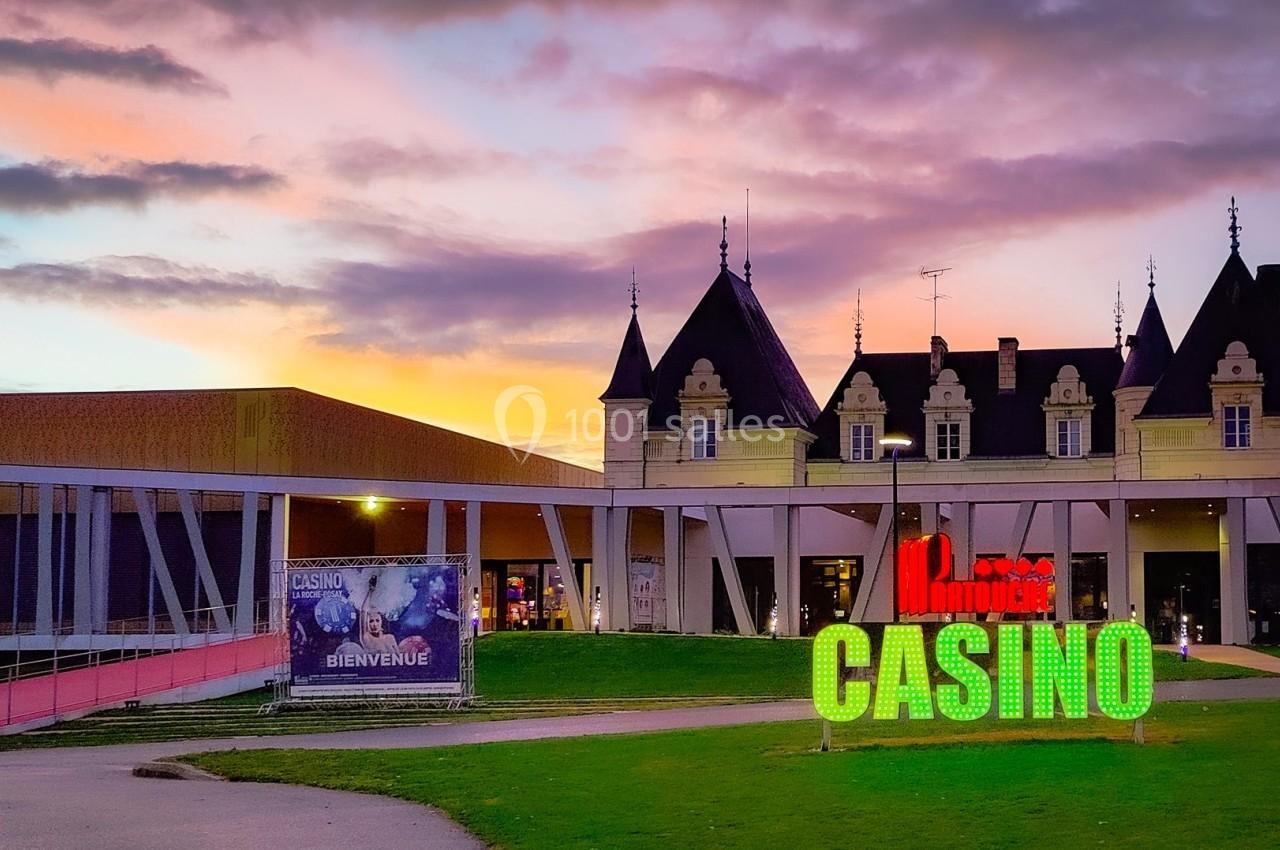 Façade d'un casino avec enseigne lumineuse, devant un bâtiment de style château au coucher du soleil.