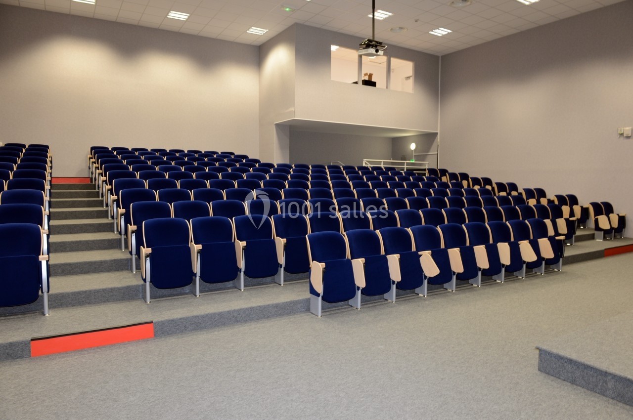 Salle de conférence vide avec des rangées de sièges bleus et un projecteur suspendu au plafond.