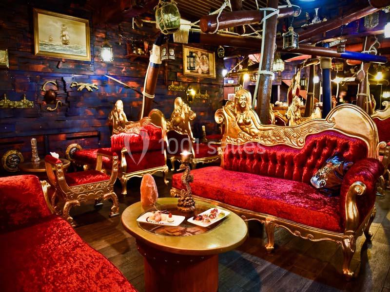 Salon au décor baroque avec canapés rouges en velours, sculptures dorées et ambiance chaleureuse.