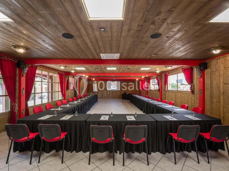Salle de réunion spacieuse avec tables en U, chaises rouges, écran de projection et lumière naturelle.