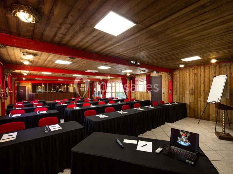 Salle de réunion avec tables alignées, chaises rouges, paperboards et matériel de présentation dans un décor en bois.
