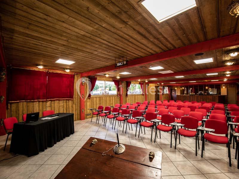 Salle de conférence avec chaises rouges, tables équipées de micros et écran de projection, décor en bois.