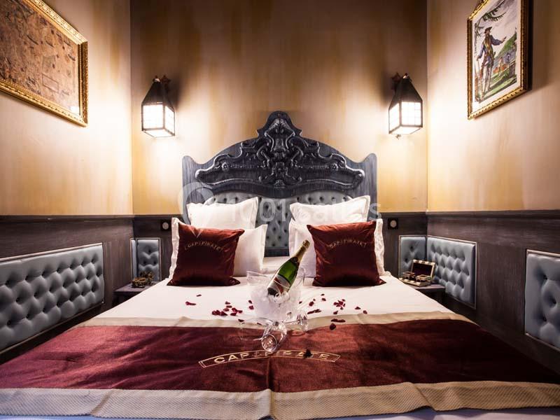 Lit double avec tête de lit sculptée, draps rouges, pétales de rose, bouteille de champagne et éclairage tamisé.