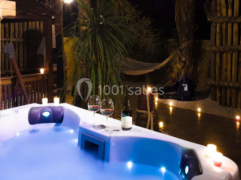 Deux verres de vin et une bouteille posés sur un jacuzzi éclairé, entouré de bougies et de végétation tropicale.