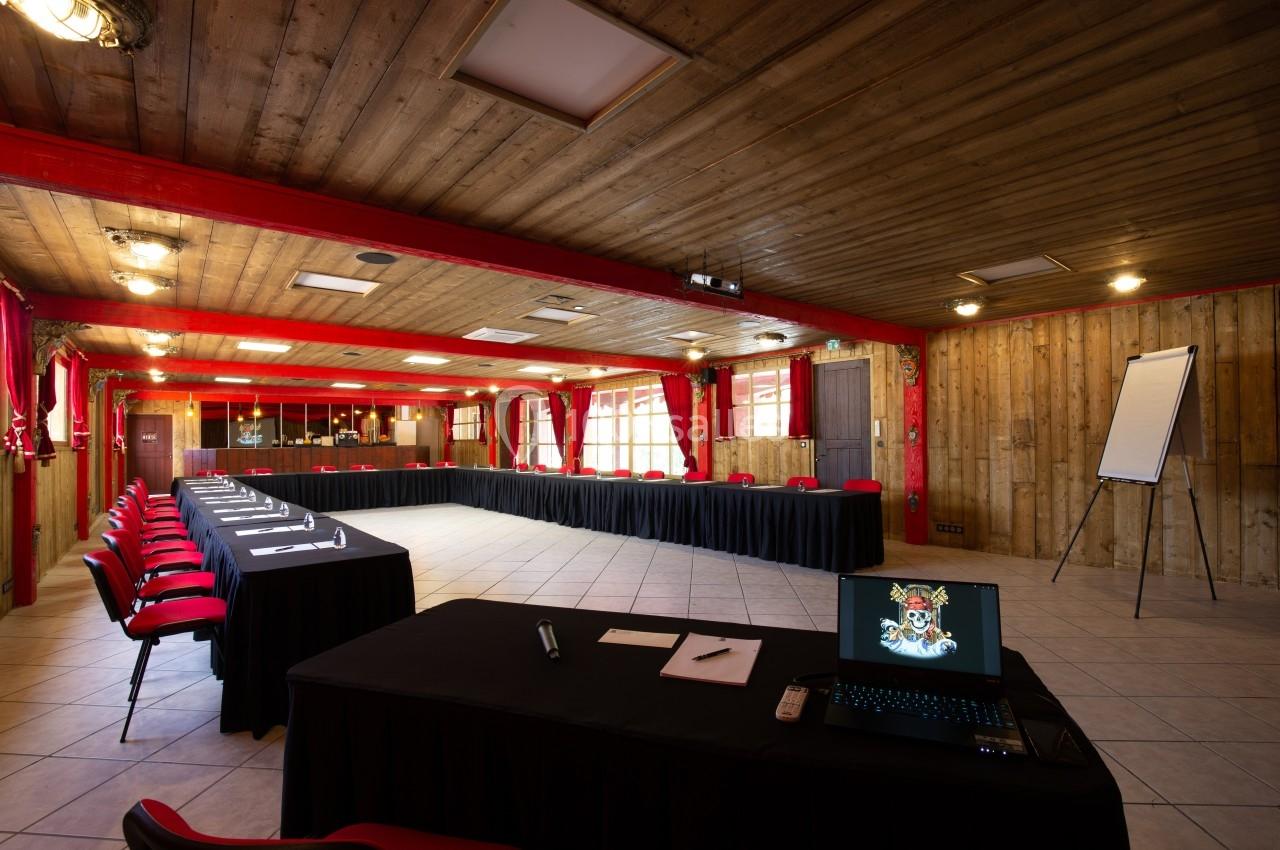 Salle de réunion spacieuse avec tables en U, chaises rouges, paperboard et ordinateur portable sur une table.
