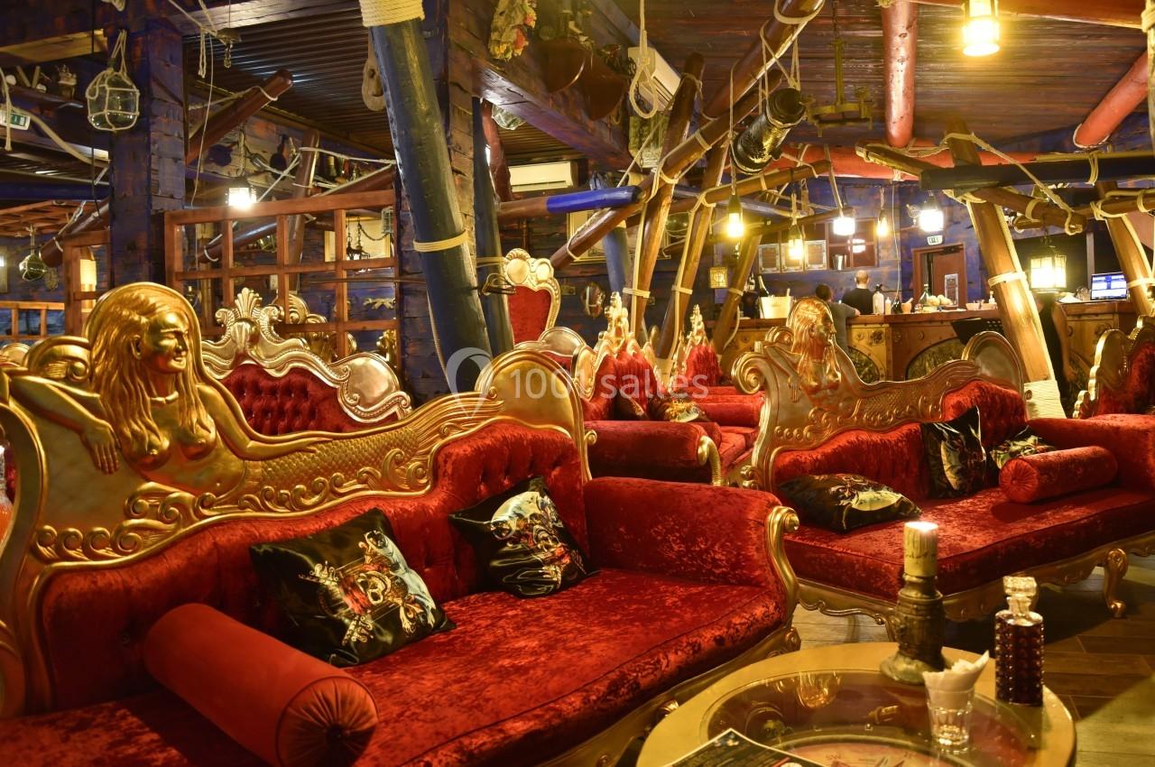 Salon décoré de façon éclectique avec des canapés rouges ornés de sculptures dorées et un éclairage chaleureux.