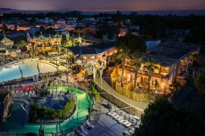 Vue nocturne d'un complexe de loisirs avec piscine illuminée, bâtiments thématiques et paysage urbain en arrière-plan.