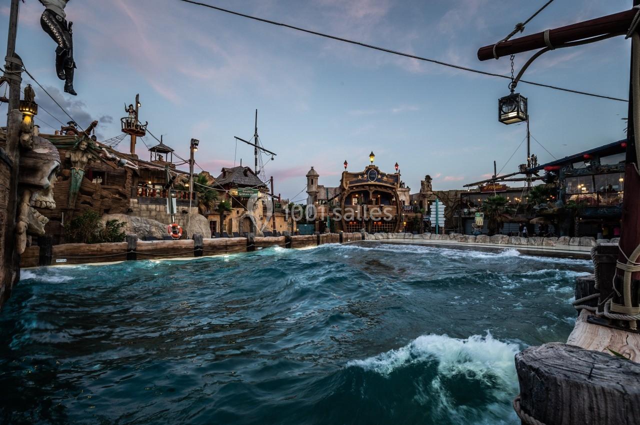 Vue d'une attraction aquatique à thème pirate avec des bâtiments décoratifs et des vagues artificielles au crépuscule.