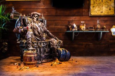 Vue nocturne d'un complexe de loisirs avec piscine illuminée, bâtiments thématiques et paysage urbain en arrière-plan.