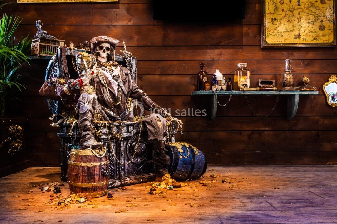 Un squelette de pirate assis sur un trône entouré de trésors, dans une pièce décorée de cartes et d'objets marins.