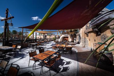 Vue nocturne d'un complexe de loisirs avec piscine illuminée, bâtiments thématiques et paysage urbain en arrière-plan.