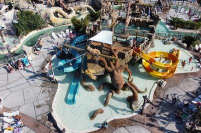 Vue nocturne d'un complexe de loisirs avec piscine illuminée, bâtiments thématiques et paysage urbain en arrière-plan.
