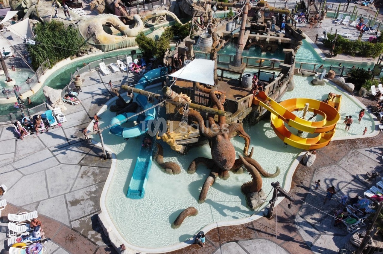 Vue aérienne d'un parc aquatique avec toboggans colorés, piscine peu profonde et décorations en forme de pieuvre.