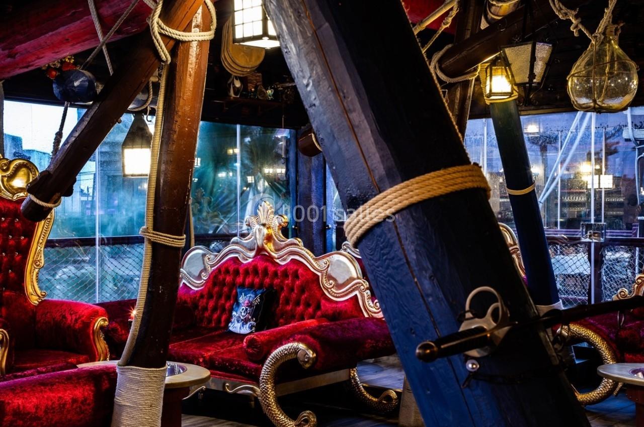 Banquettes rouges ornées et poutres en bois décorées dans un intérieur au style nautique et baroque.