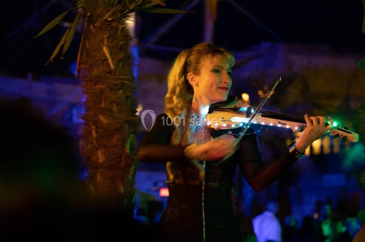 Une musicienne joue du violon lumineux dans une ambiance nocturne festive, entourée de lumières colorées.