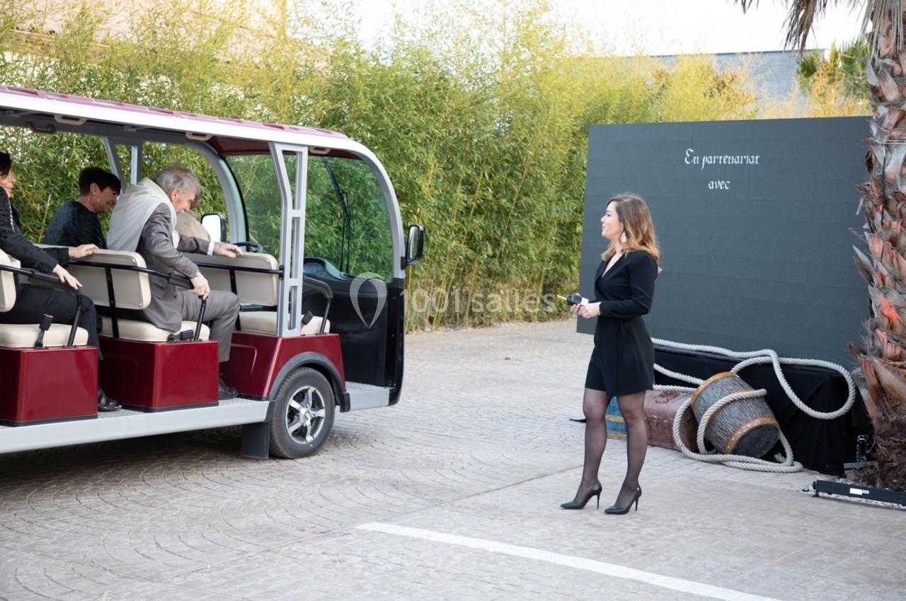 Une femme en tenue professionnelle se tient près d'une navette électrique où des passagers montent.