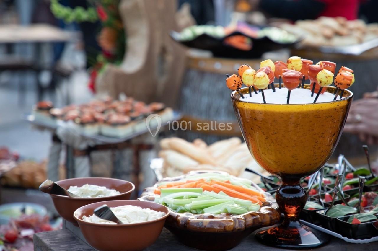 Buffet avec légumes frais, sauces en bols, et brochettes colorées présentées dans une coupe orange.