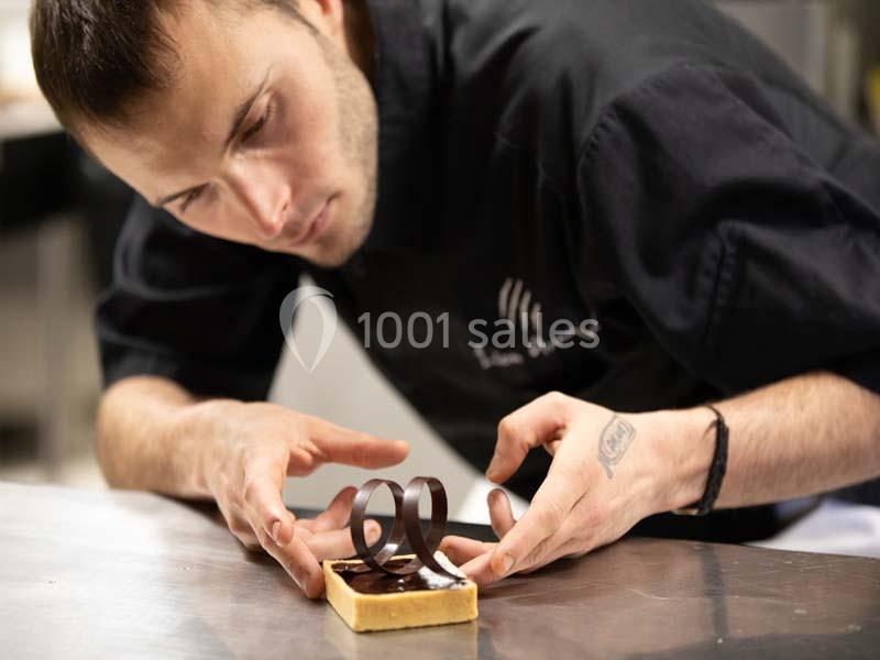 Un pâtissier décore un dessert avec précision en ajoutant des éléments en chocolat sur une surface en acier inoxydable.