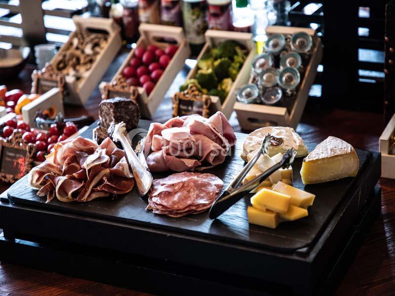 Plateau de charcuterie et fromages variés sur une table, accompagné de garnitures et condiments en arrière-plan.