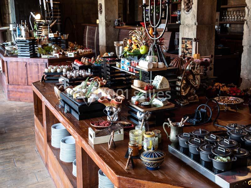 Buffet varié avec fromages, fruits, desserts et plats chauds disposés sur une table en bois dans un cadre rustique.