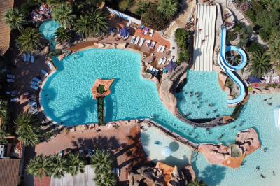 Vue nocturne d'un complexe de loisirs avec piscine illuminée, bâtiments thématiques et paysage urbain en arrière-plan.