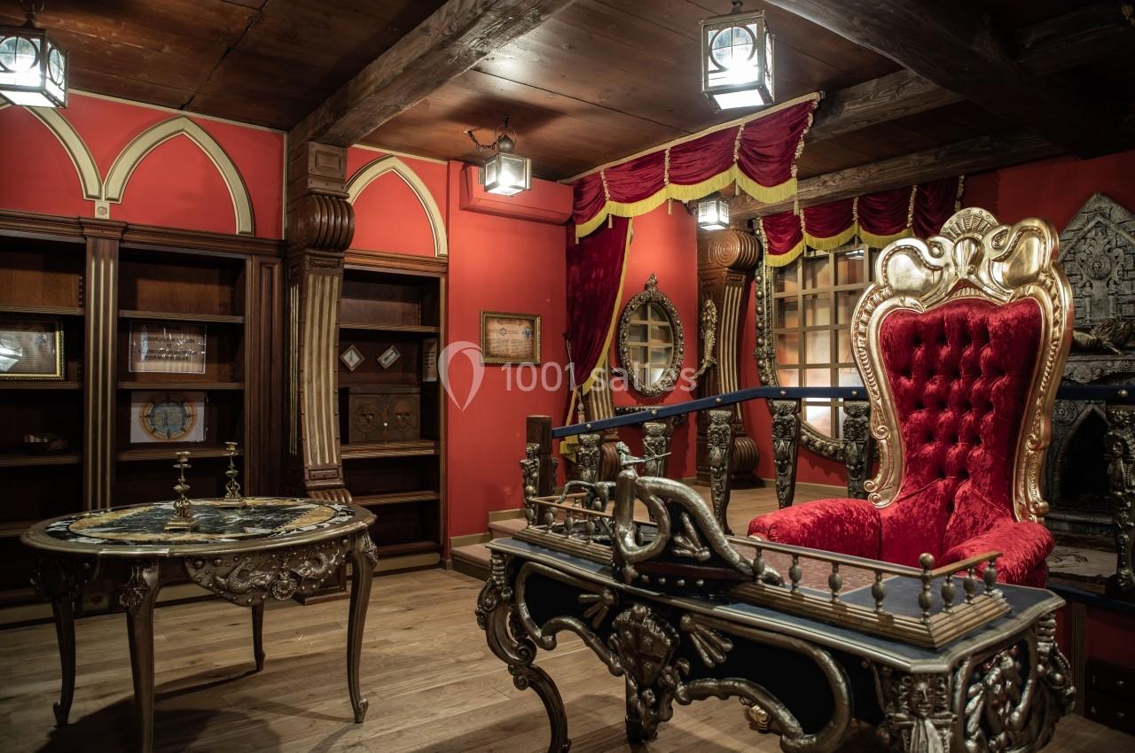 Salle décorée dans un style baroque avec meubles en bois sculpté, fauteuil rouge capitonné et rideaux rouges ornés.