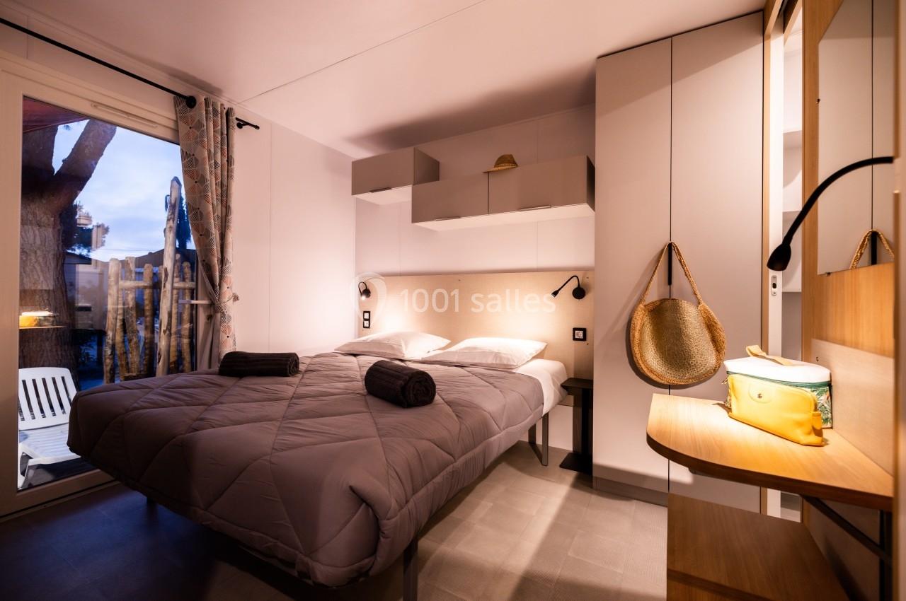 Chambre lumineuse avec lit double, draps gris, rangements intégrés, et vue sur une terrasse extérieure.