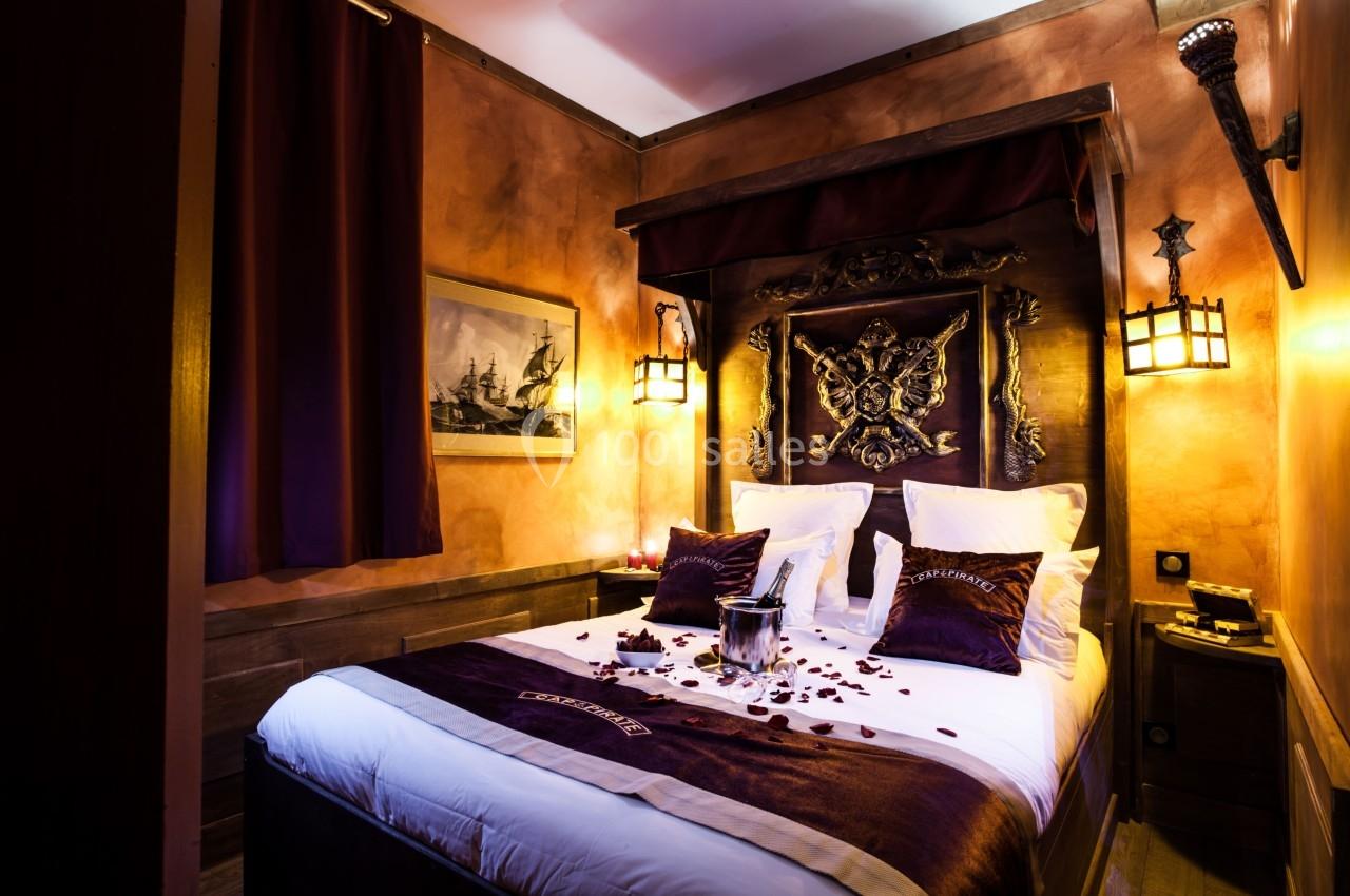 Lit double avec draps blancs, décor romantique avec pétales de rose, éclairage tamisé et ambiance chaleureuse.