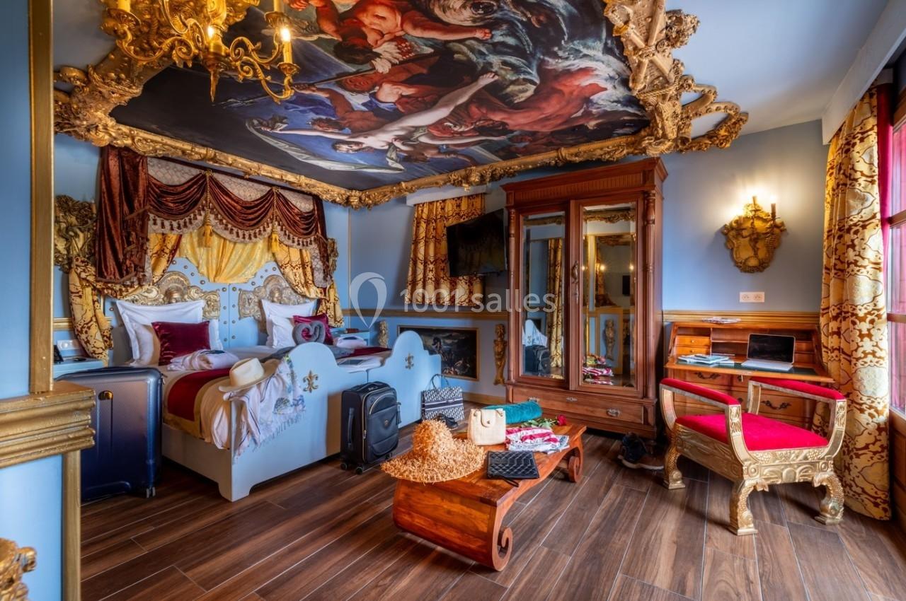 Chambre luxueuse décorée de manière baroque avec lit à baldaquin, fresque au plafond et mobilier doré.