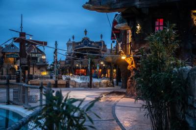 Vue nocturne d'un complexe de loisirs avec piscine illuminée, bâtiments thématiques et paysage urbain en arrière-plan.