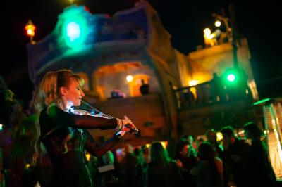 Vue nocturne d'un complexe de loisirs avec piscine illuminée, bâtiments thématiques et paysage urbain en arrière-plan.
