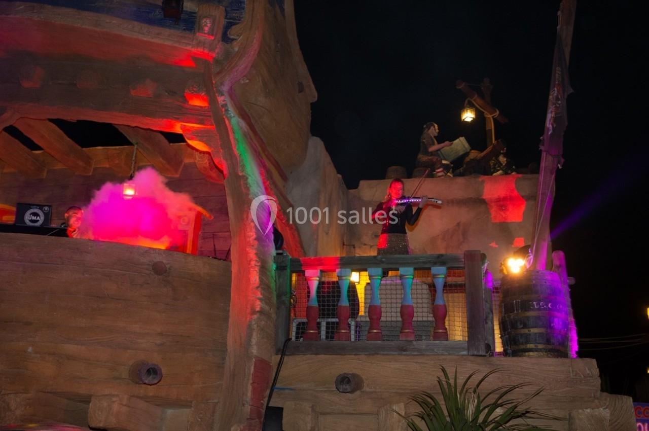 Un musicien joue du violon sur une structure en bois éclairée par des lumières colorées, de nuit.