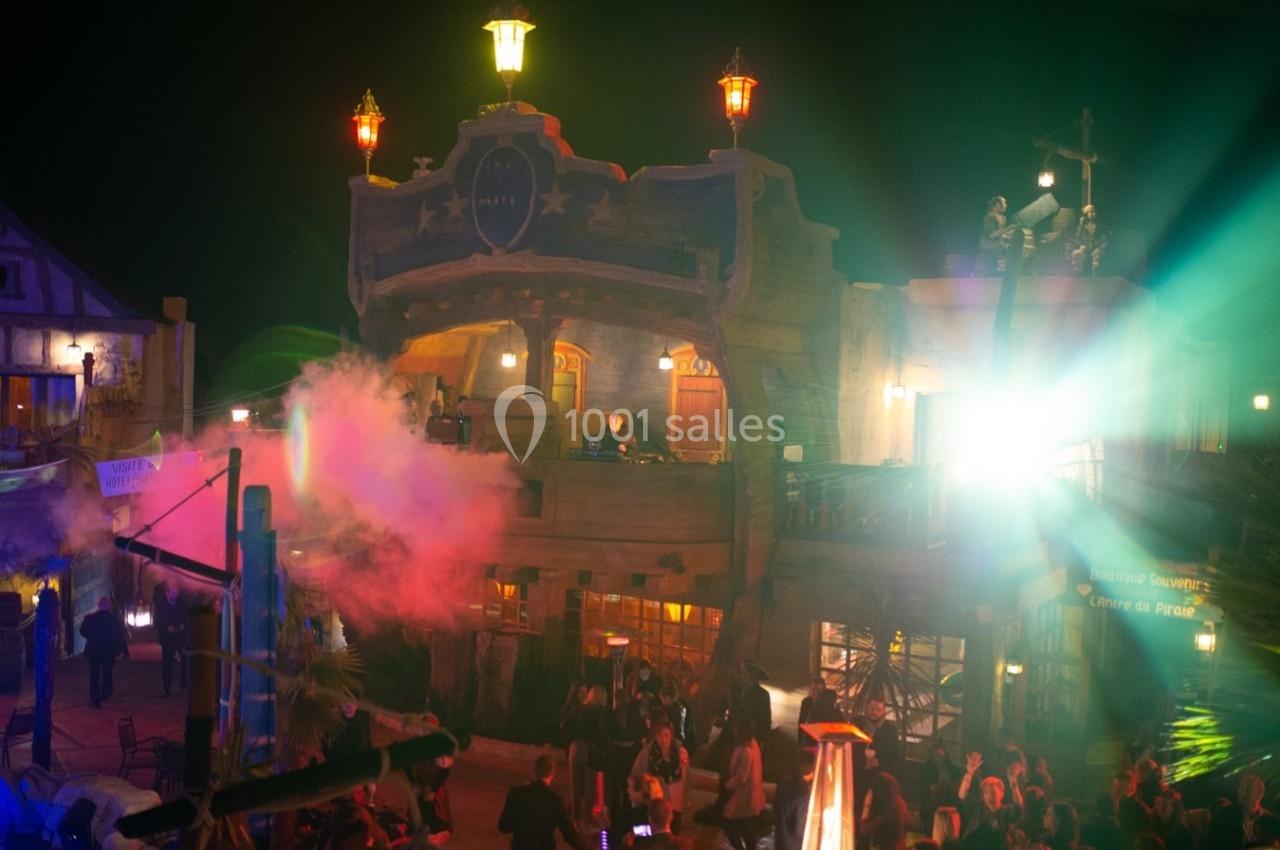 Façade éclairée d'un bâtiment à thème pirate avec des lumières colorées et une foule rassemblée de nuit.
