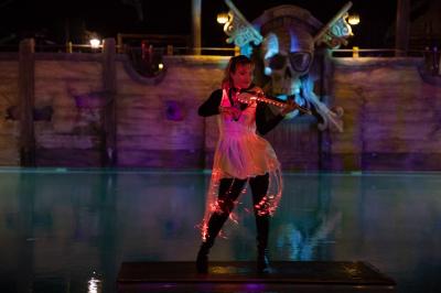 Vue nocturne d'un complexe de loisirs avec piscine illuminée, bâtiments thématiques et paysage urbain en arrière-plan.