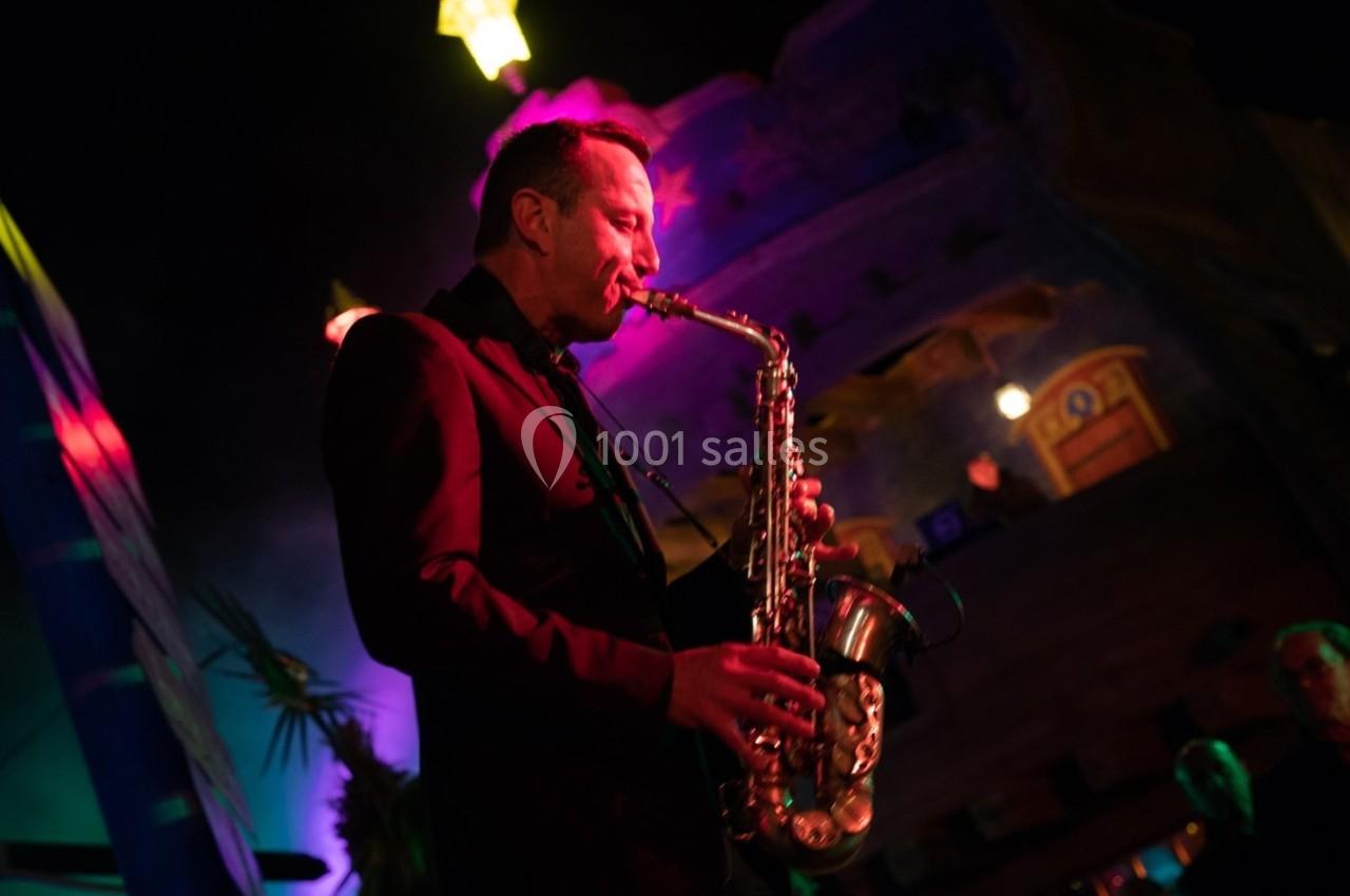 Un musicien joue du saxophone sous des lumières colorées dans une ambiance nocturne.