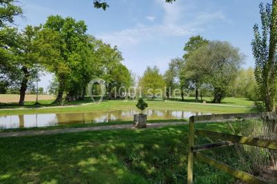 Paysage champêtre avec un étang entouré d'arbres, une barrière en bois au premier plan et un ciel dégagé.