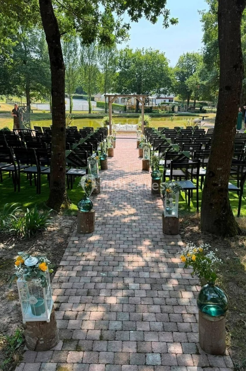 Allée pavée bordée de décorations florales menant à une arche en bois, avec des chaises disposées pour une cérémonie.