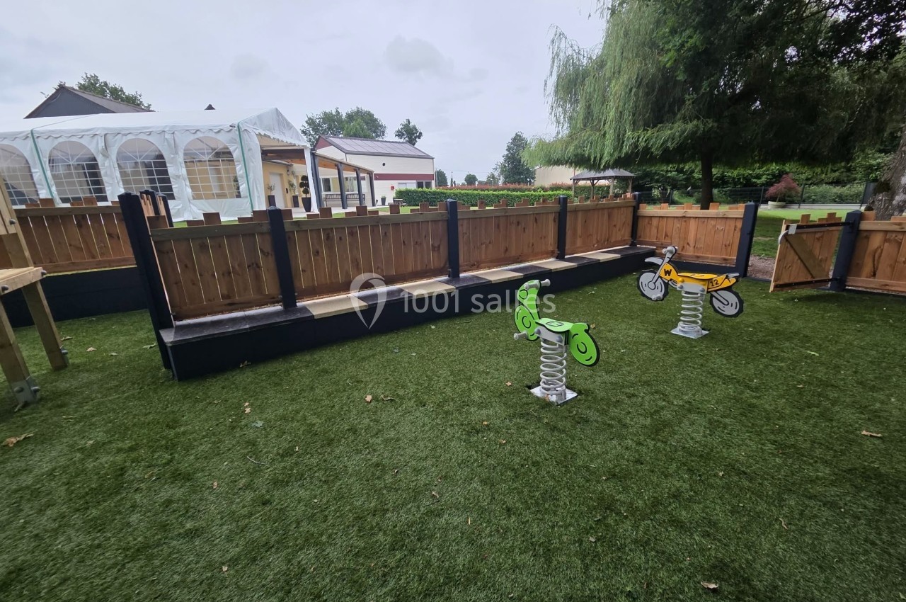 Jeux à ressort pour enfants sur une pelouse artificielle, entourés de clôtures en bois et d'arbres en arrière-plan.