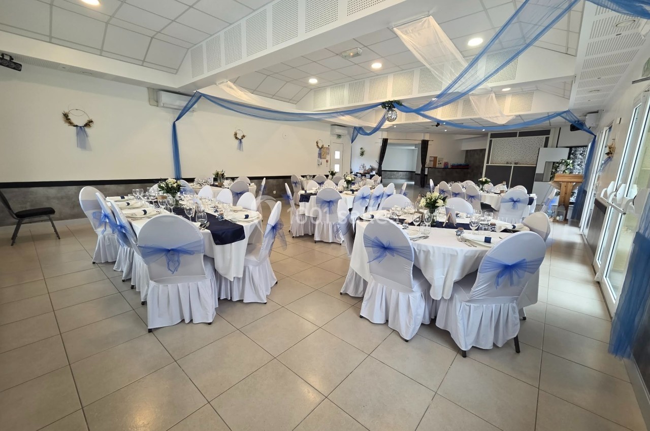 Salle de réception décorée en bleu et blanc avec tables dressées et chaises ornées de nœuds bleus.