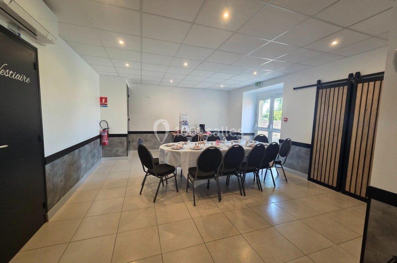 Salle lumineuse avec table ronde dressée pour un repas, entourée de chaises noires, dans un cadre sobre et moderne.