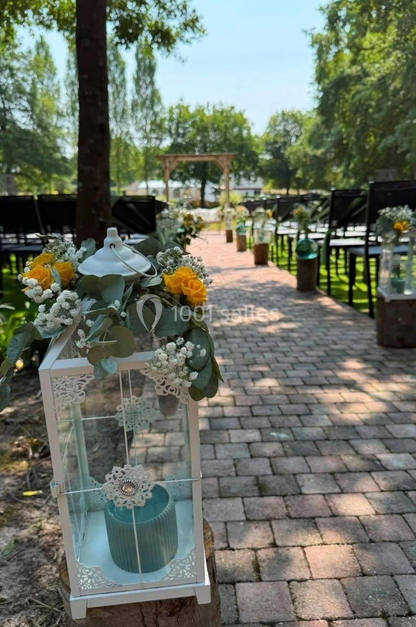 Allée extérieure pavée décorée pour une cérémonie, avec lanternes blanches ornées de fleurs jaunes et blanches.