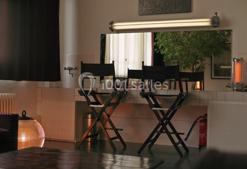 Trois chaises de réalisateur devant un miroir éclairé, dans une pièce avec une plante et une décoration chaleureuse.