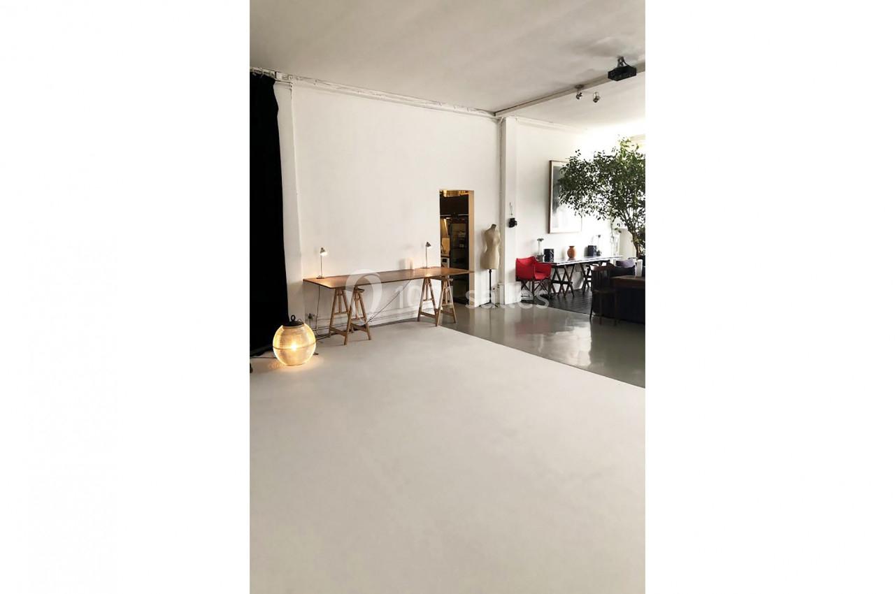 Salle lumineuse avec un bureau en bois, une lampe au sol, un canapé et une grande plante dans un espace ouvert.