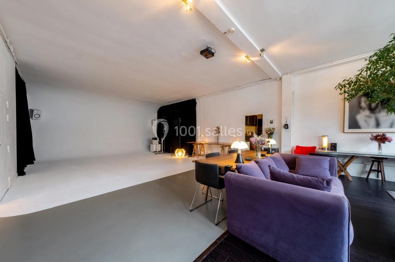 Espace intérieur lumineux avec un studio photo, canapé violet, table en bois et décoration moderne.