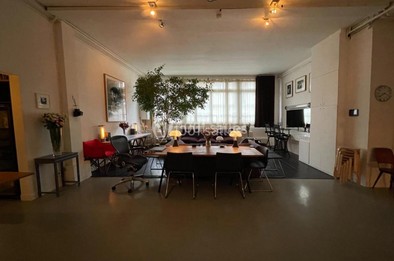 Espace intérieur lumineux avec grande table en bois, chaises noires, plantes, et mobilier moderne dans un cadre épuré.