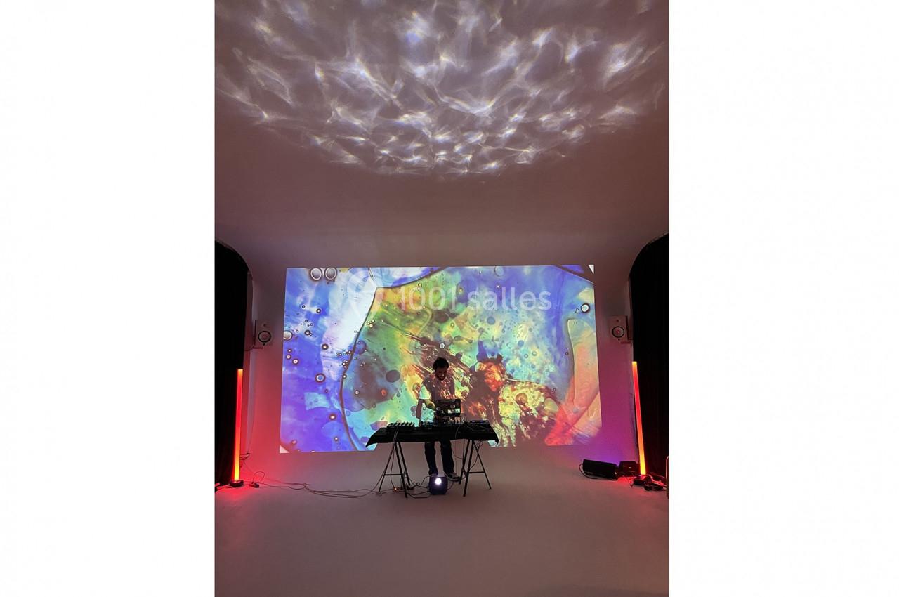 Un DJ mixe sur une table de sonorisation devant une projection colorée dans une pièce sombre.