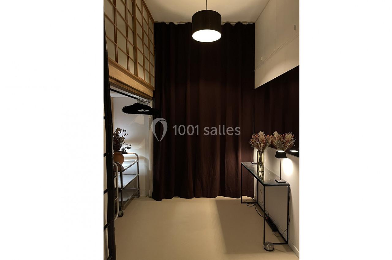 Espace intérieur avec rideaux sombres, éclairage suspendu, console avec décorations et étagère avec cintres.