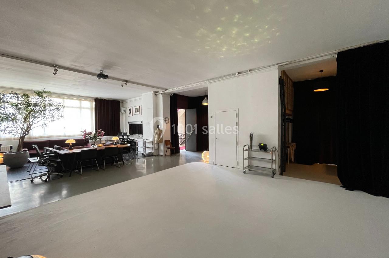 Espace intérieur lumineux avec un grand salon, une table à manger, des plantes et des rideaux noirs en arrière-plan.