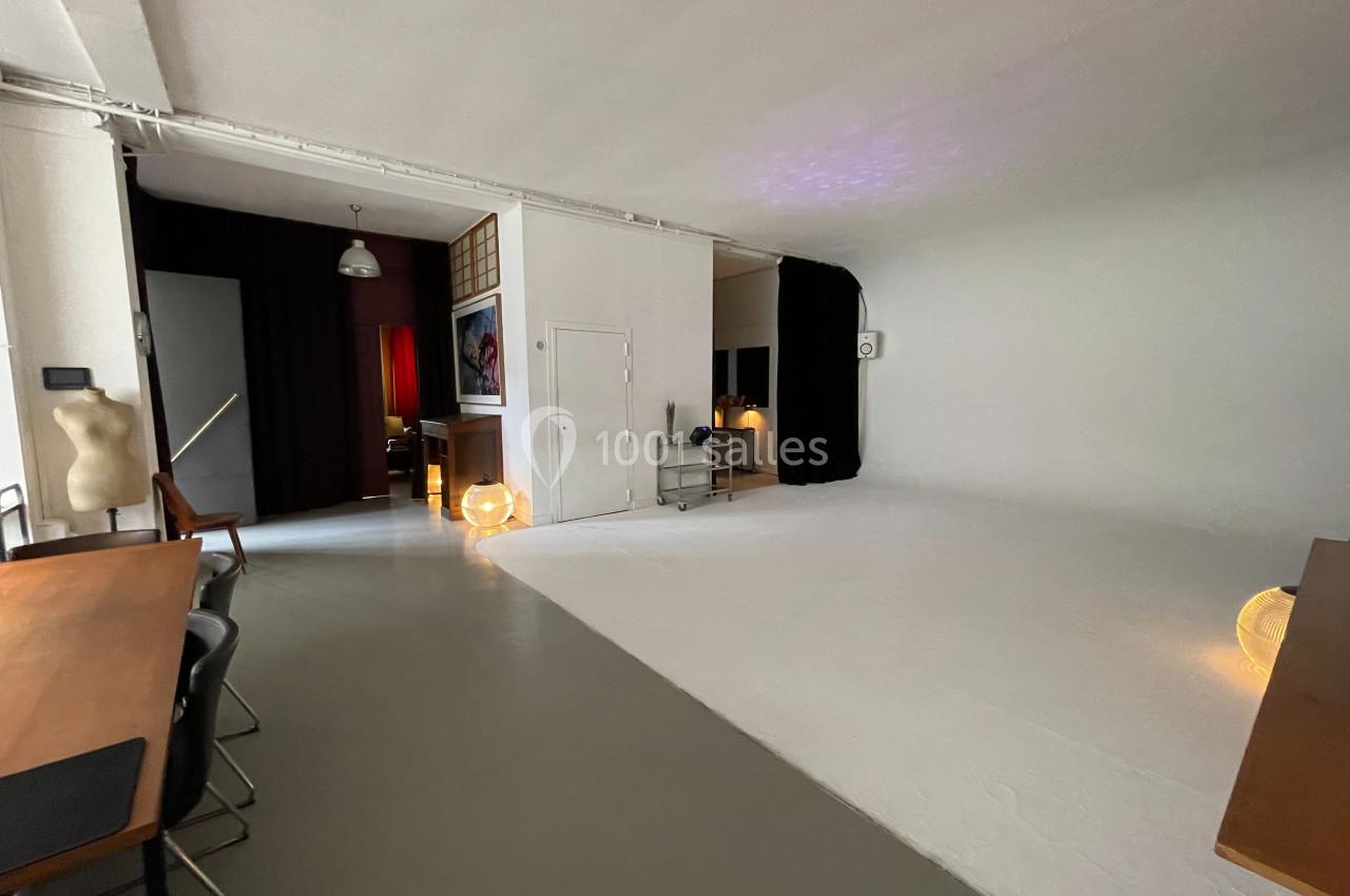 Studio lumineux avec fond blanc, mobilier minimaliste, mannequins et éclairage tamisé dans un espace polyvalent.