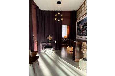 Grand arbre en pot éclairé par une lumière verte dans un salon moderne avec canapé, tables et vases de fleurs.